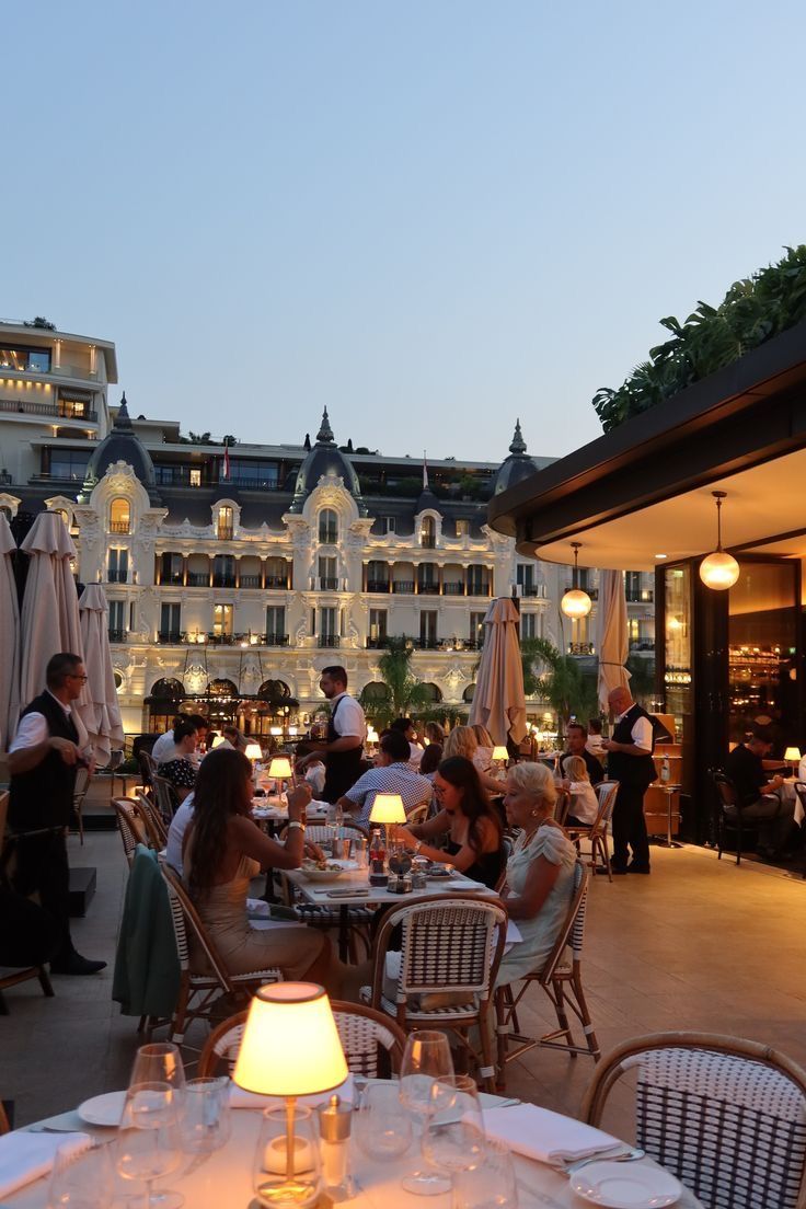 Terrace restaurant in Monte-Carlo at dusk facing the Hôtel de Paris facade, tables lit by small lamps