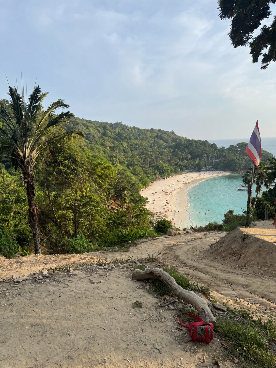 Tropical bay with white sand beach, turquoise water and lush green hills seen from a shaded path
