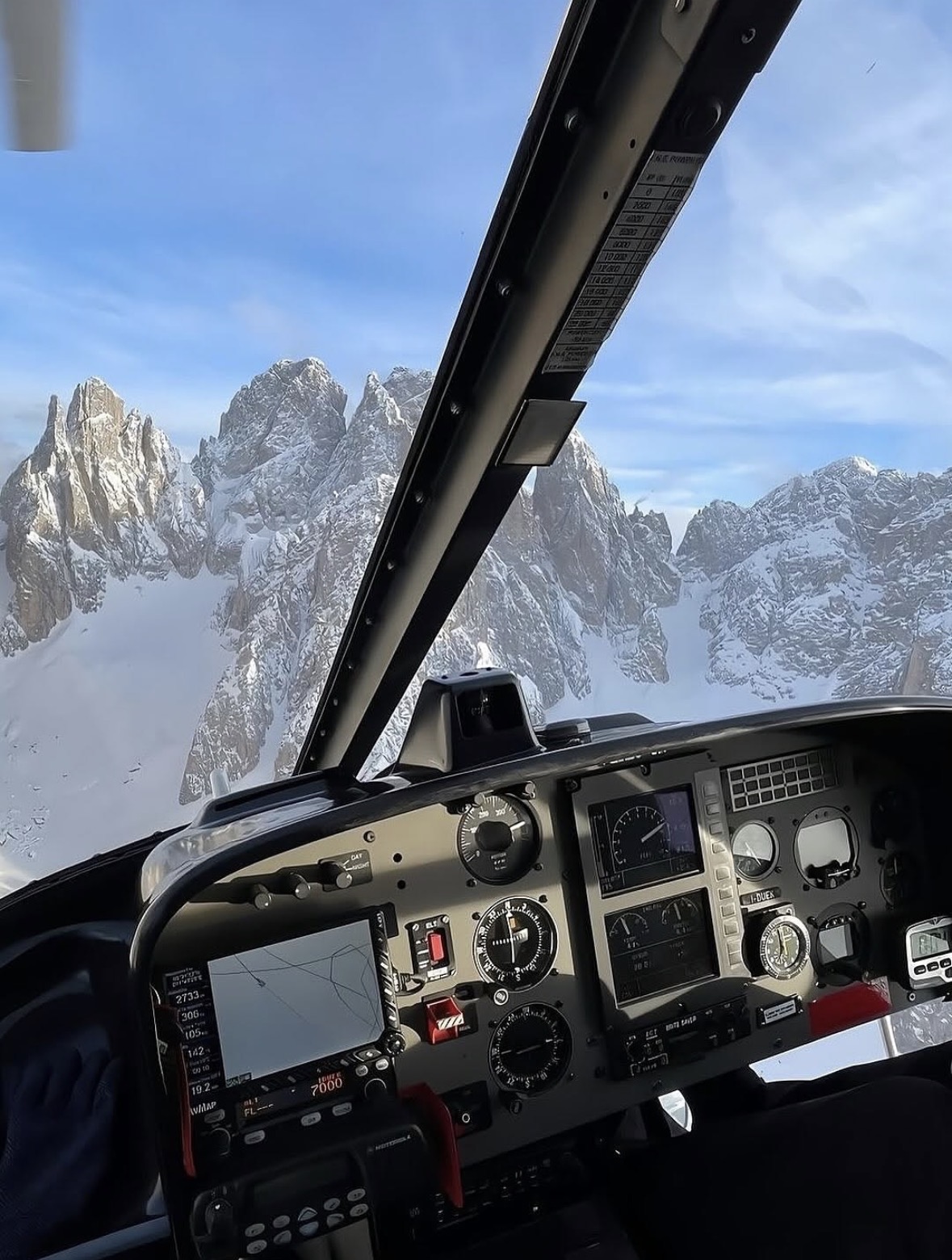 View from a helicopter cockpit flying past snow-covered alpine rock spires